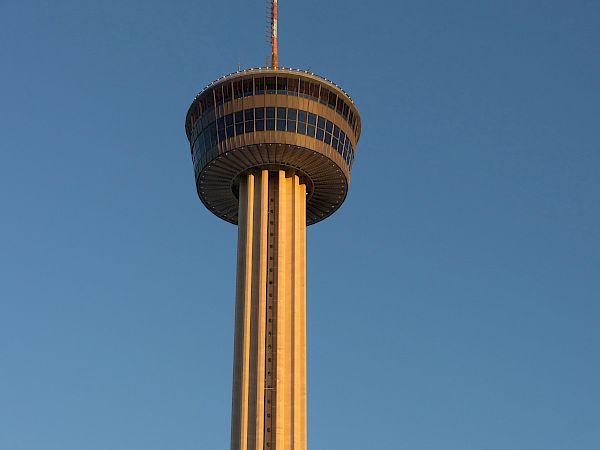 A tall observation tower rises against a clear blue sky, with a small crescent moon visible above near the upper right corner.