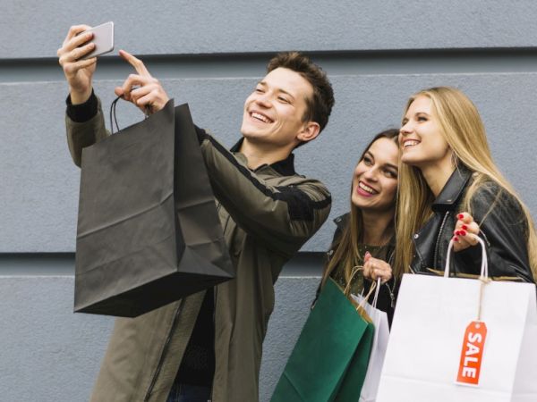 Three friends take a selfie with shopping bags after a sale, posing happily.
