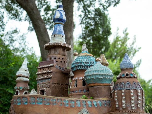Colorful miniature castle-like structures with domed roofs, towers, and brick textures set among trees, resembling an artistic clay model.