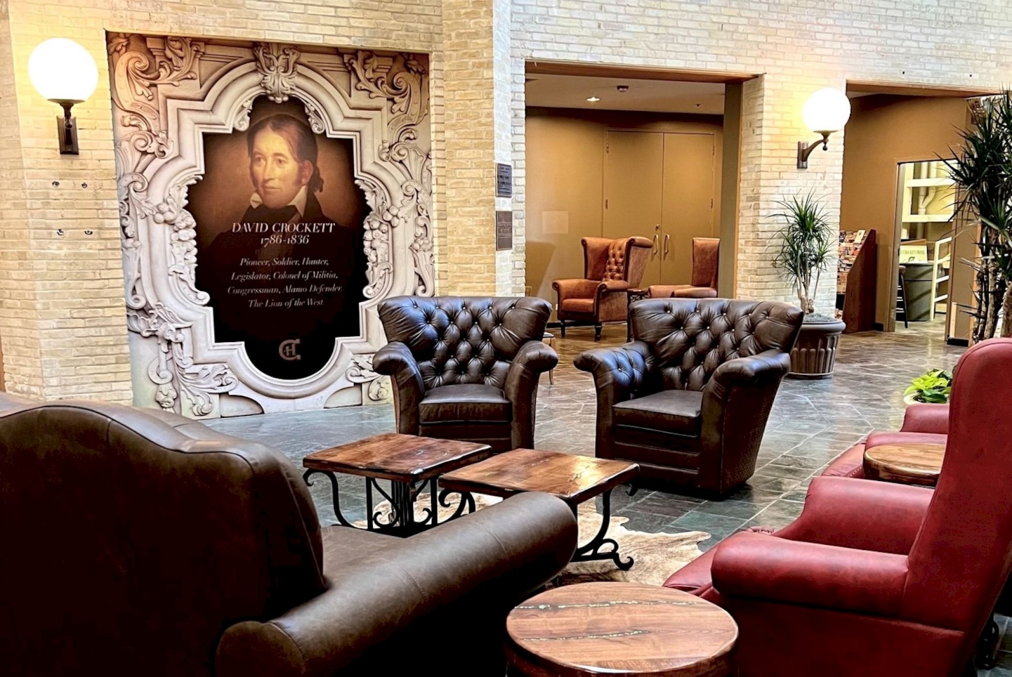 A chic lounge area with tufted leather chairs, wooden tables, and warm lighting in an elegant hotel lobby, featuring a decorative arched panel and artwork.